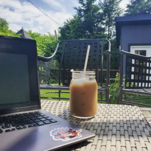 A laptop and an iced coffee on the table in an outdoor patio.